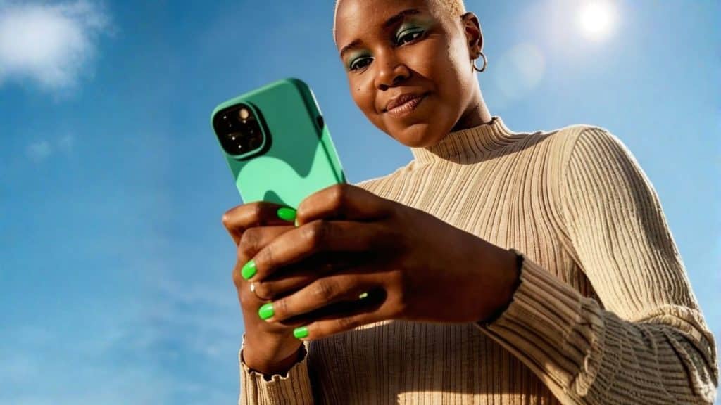 Mulher usando smartphone ao ar livre, com foco na tela do dispositivo, representando comportamento digital mobile, consumo de conteúdo em tempo real e interação com plataformas online